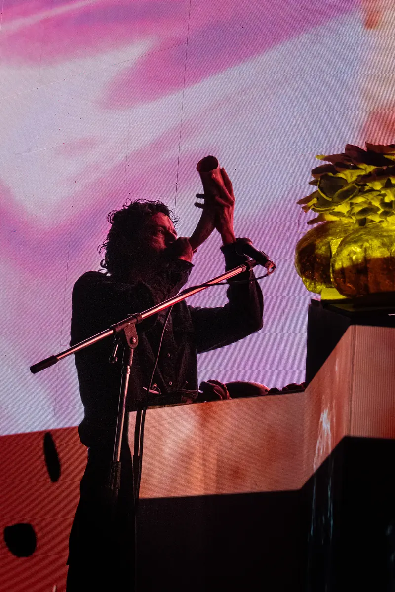 Darvin Elisondo de perfil, inclinado sobre sus instrumentos, contra una visual rosa y roja