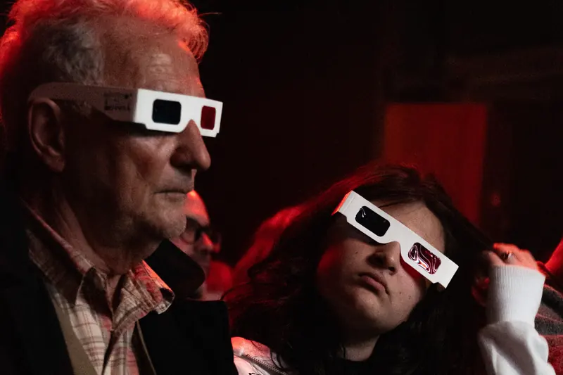 Dos espectadores con lentes 3D de cartón en la sala de ArtLab, un hombre de pelo blanco y una joven de pelo enrulado