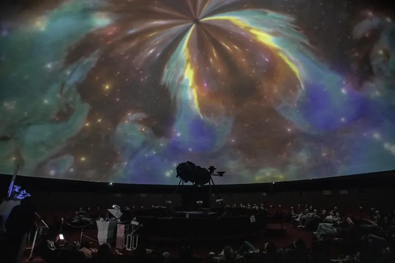 El domo del Planetario de Rosario con una nebulosa proyectada y la platea llena