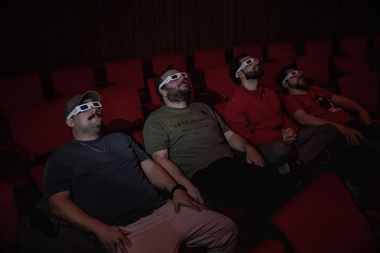 Cuatro espectadores con lentes 3D, recostados en las butacas, miran la cúpula del planetario