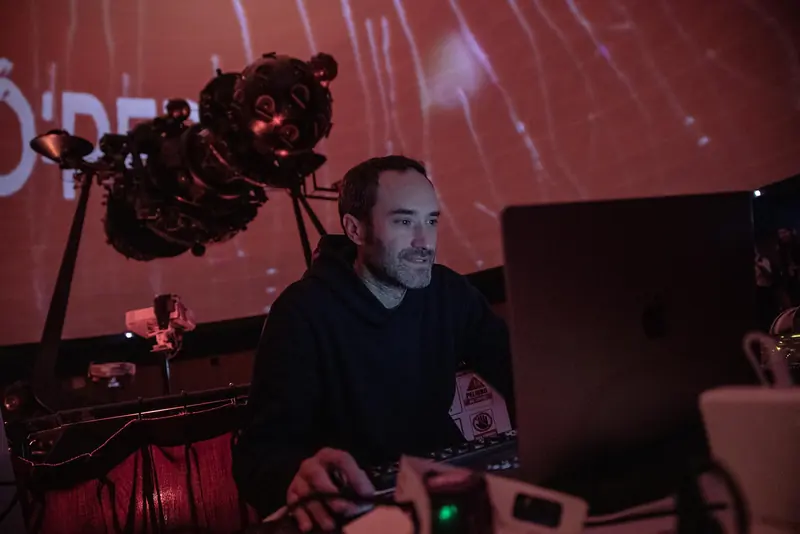Integrante sonriente frente a su computadora, con el proyector estelar del planetario en primer plano